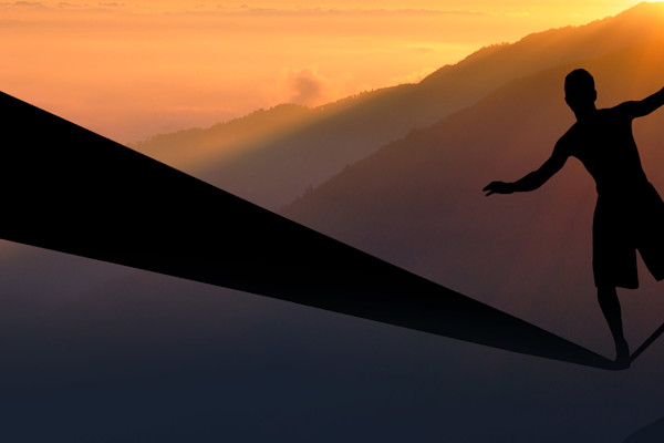 Silhouette of a person balancing on a slackline above a ridge of hills at sunset.